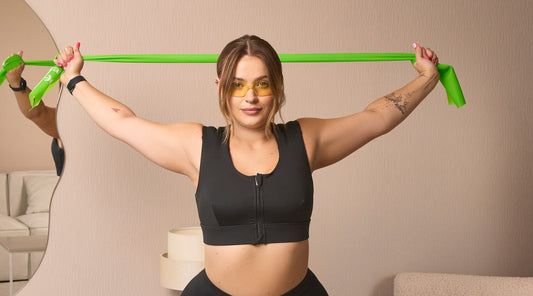 A woman in the Etalon posture bra using a green body posture band for upper-body flexibility.