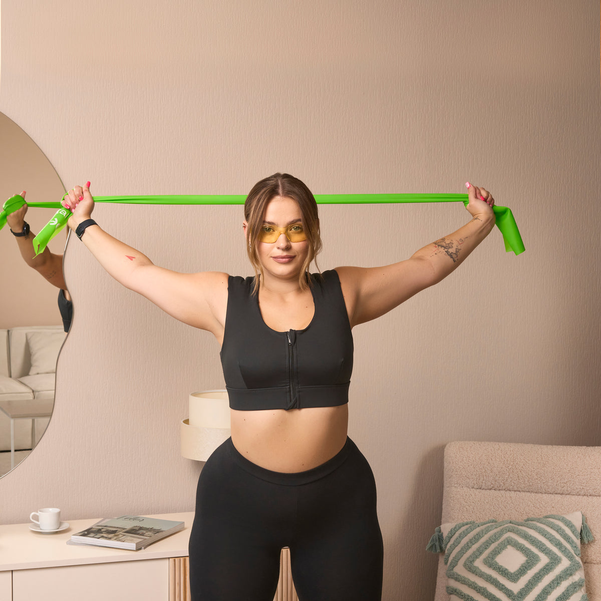 A woman in the Etalon posture bra using a green body posture band for upper-body flexibility.
