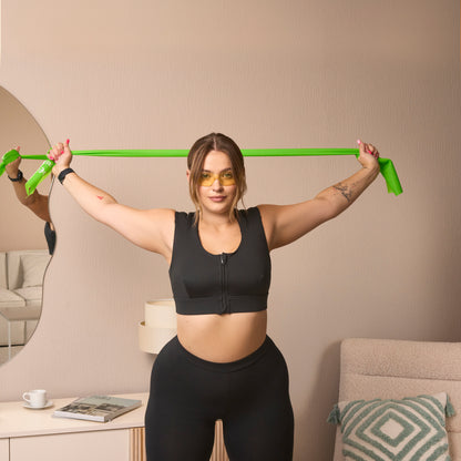 A woman in the Etalon posture bra using a green body posture band for upper-body flexibility.